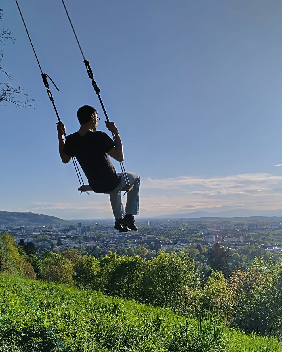 Dariush Ghiass-Fakhri auf einer Schaukel mit Stadtpanorama